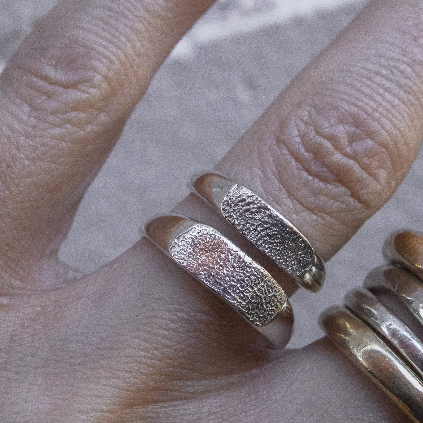 A close-up of a hand wearing textured silver rings, with one wide textured band prominently displayed on the middle finger.