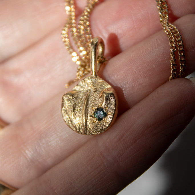 Gold cat nose print necklace with a blue gemstone, held in a hand