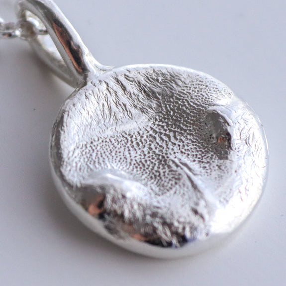 Silver cat nose pendant very close up on a light gray background