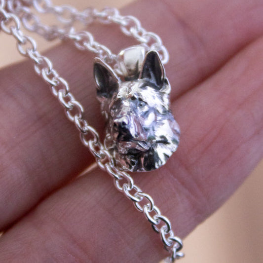 A close-up of a silver realistic german shepherd 3d pendant necklace resting on a person's fingers 