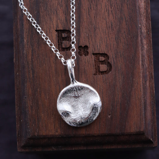 Silver circle cat nose print necklace with a pendant on a wooden display box