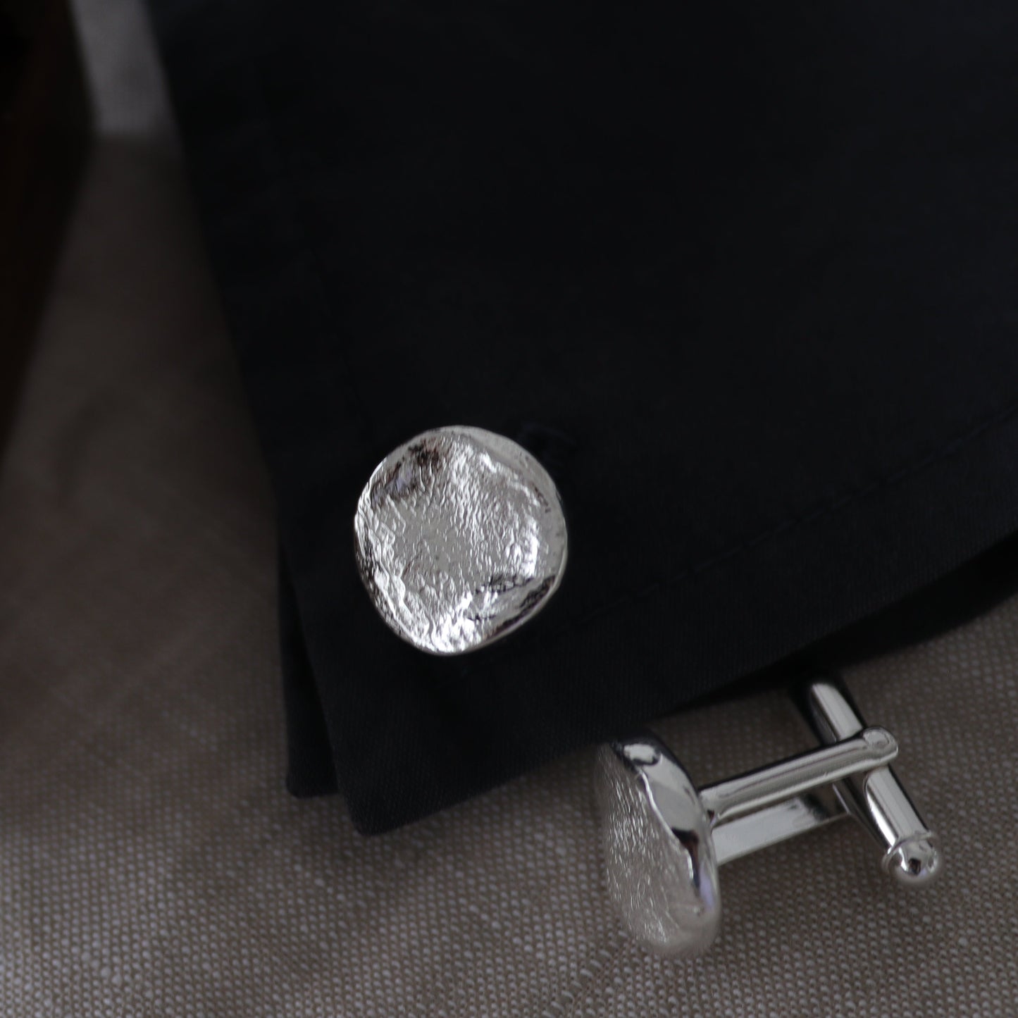 Silver cufflinks on a dark fabric background with a wooden box.