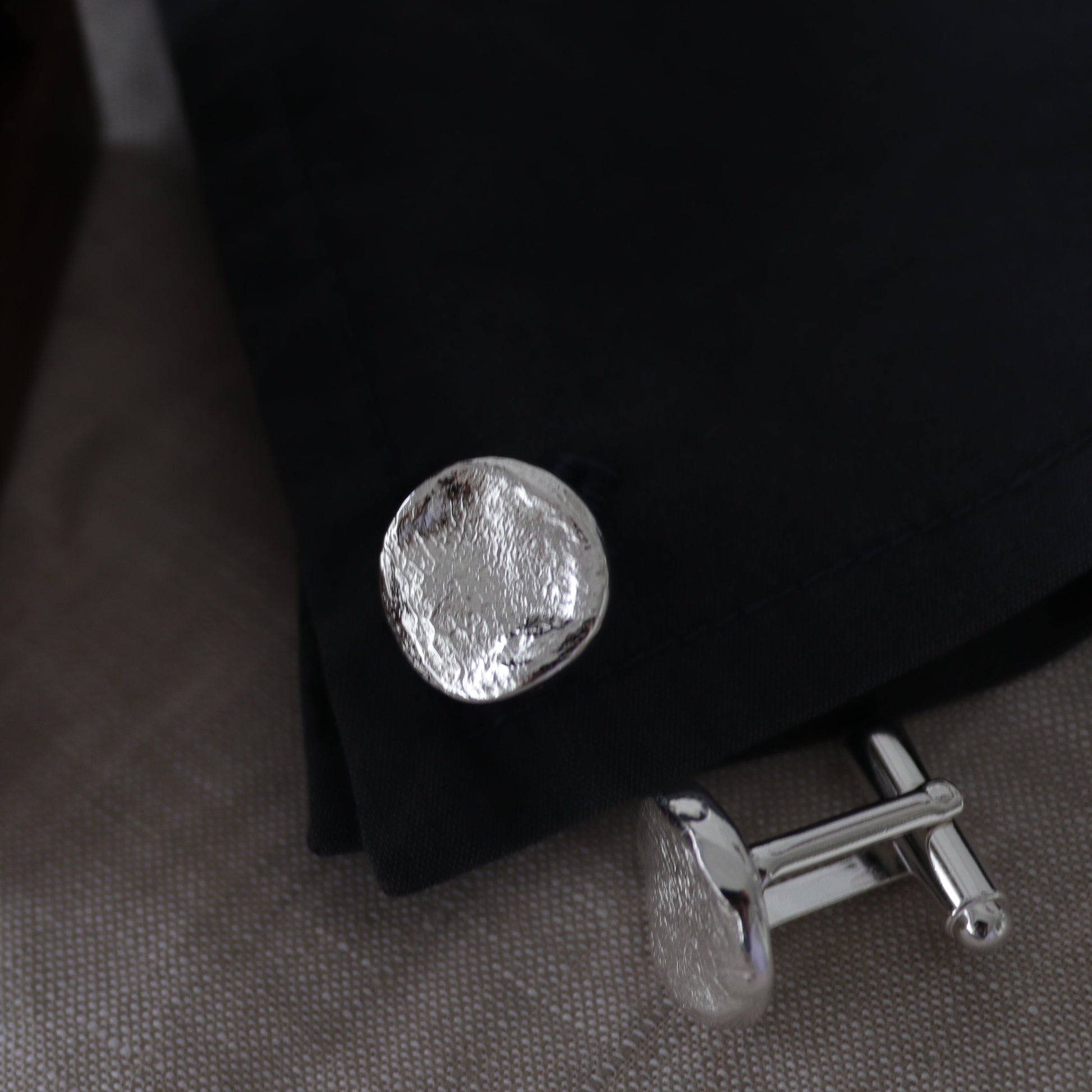 Silver cufflinks on a dark fabric background with a wooden box.