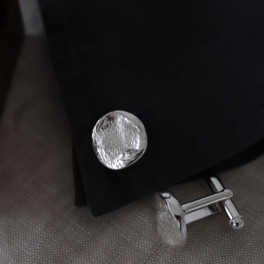 Silver cufflinks on a dark fabric background with a wooden box.