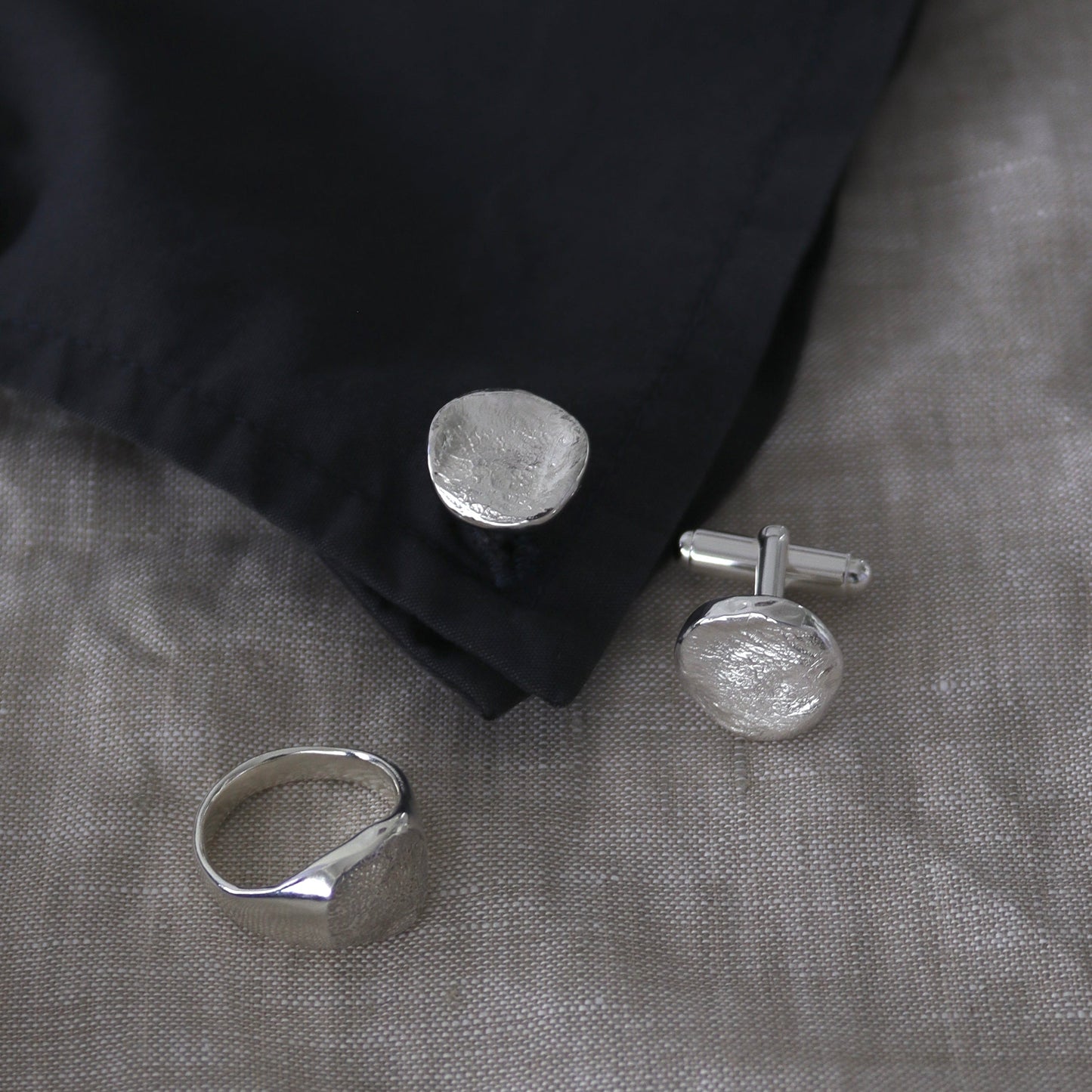 Silver dog nose print ring and cufflinks on a black fabric background