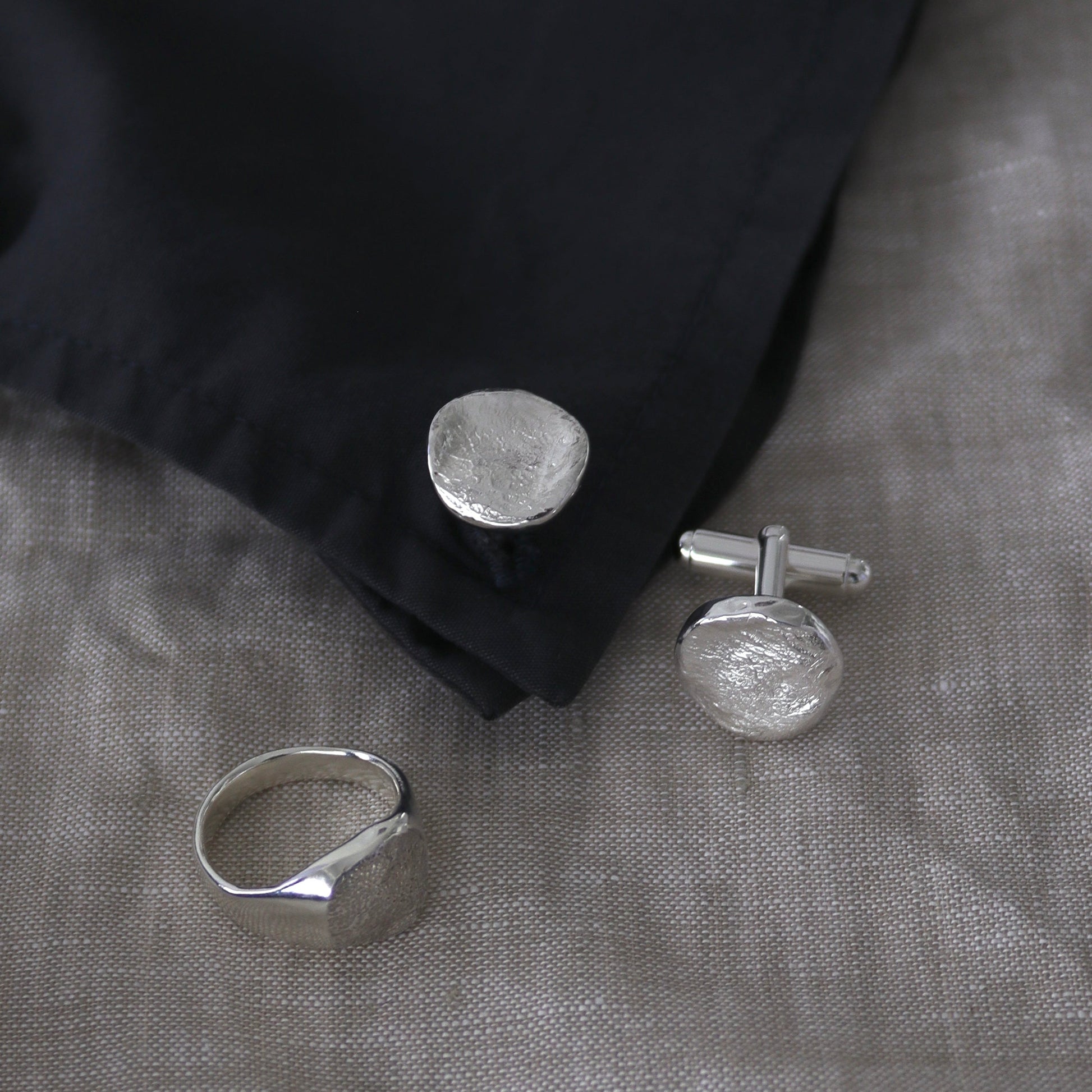 Silver dog nose print ring and cufflinks on a black fabric background