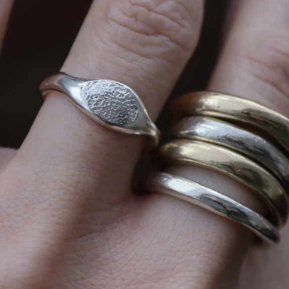A close-up of a hand wearing  a dog nose print silver ring with a leaf-like shape and stacked gold and silver bands.