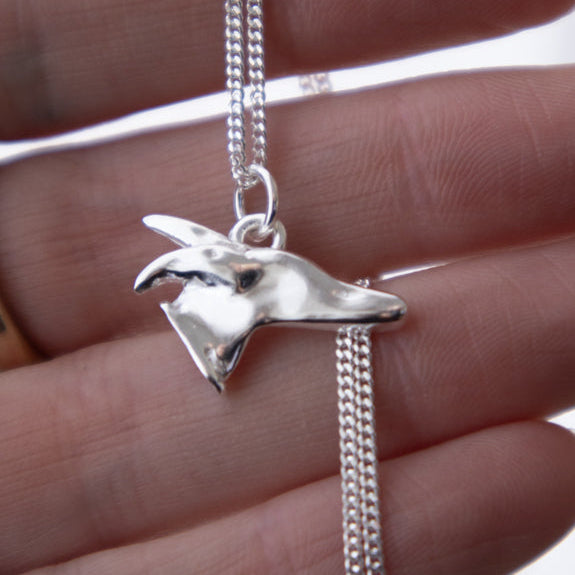 A silver necklace with a stylised greyhound head pendant, held in a person's hand against a white background.