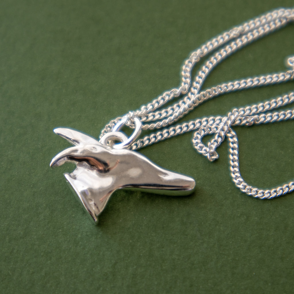 A sterling silver pendant necklace featuring a stylised greyhound head charm, displayed on a textured dark green background.