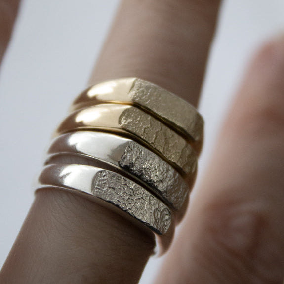 A close-up of a hand wearing a stack of dog nose print metal rings in gold and silver.